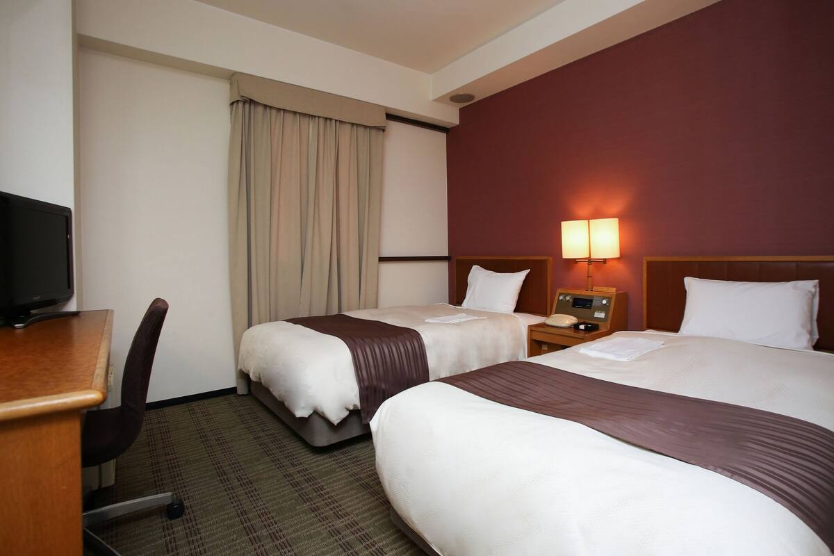 Een hotelkamer met twee bedden, een bureau, een stoel, een televisie en een lamp.