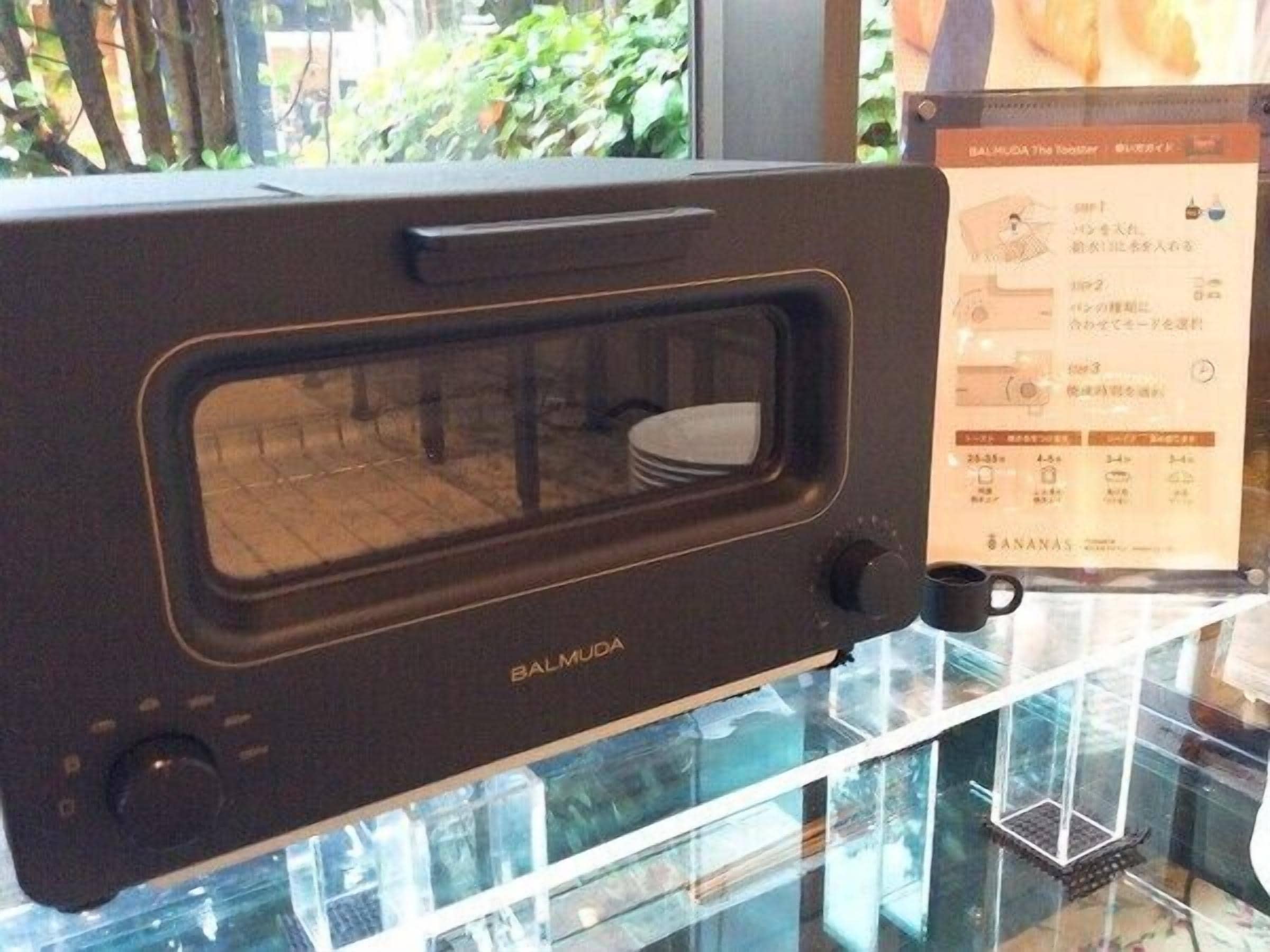 Un horno microondas negro con ventana de vidrio y panel de control, con el texto 'Balmuda'.
