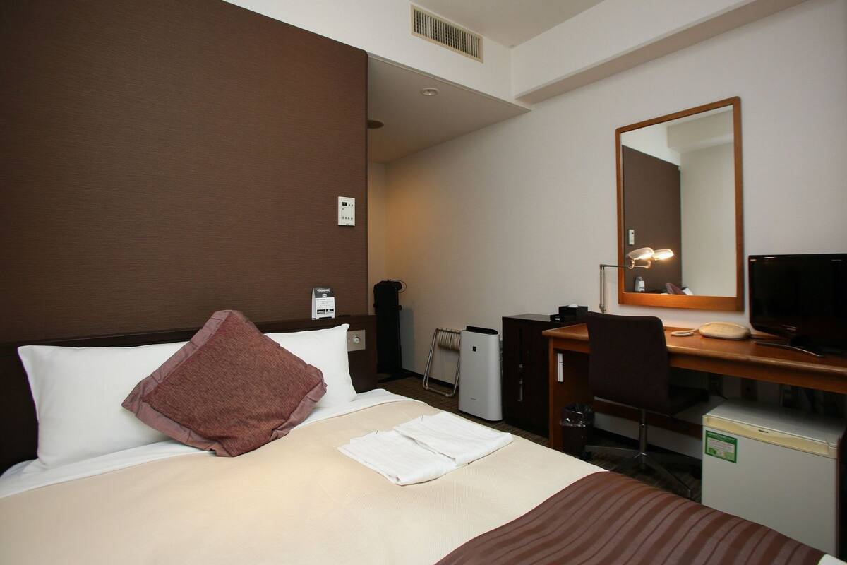 Hotelkamer met een bed, bureau, stoel, televisie en spiegel.