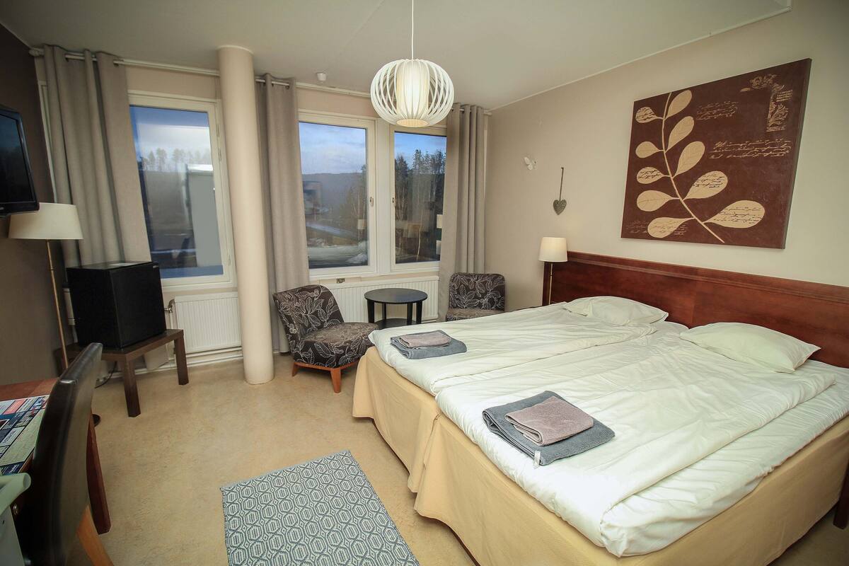 A hotel room with two beds, a TV, a desk, a chair, and a window with a view of the outdoors.