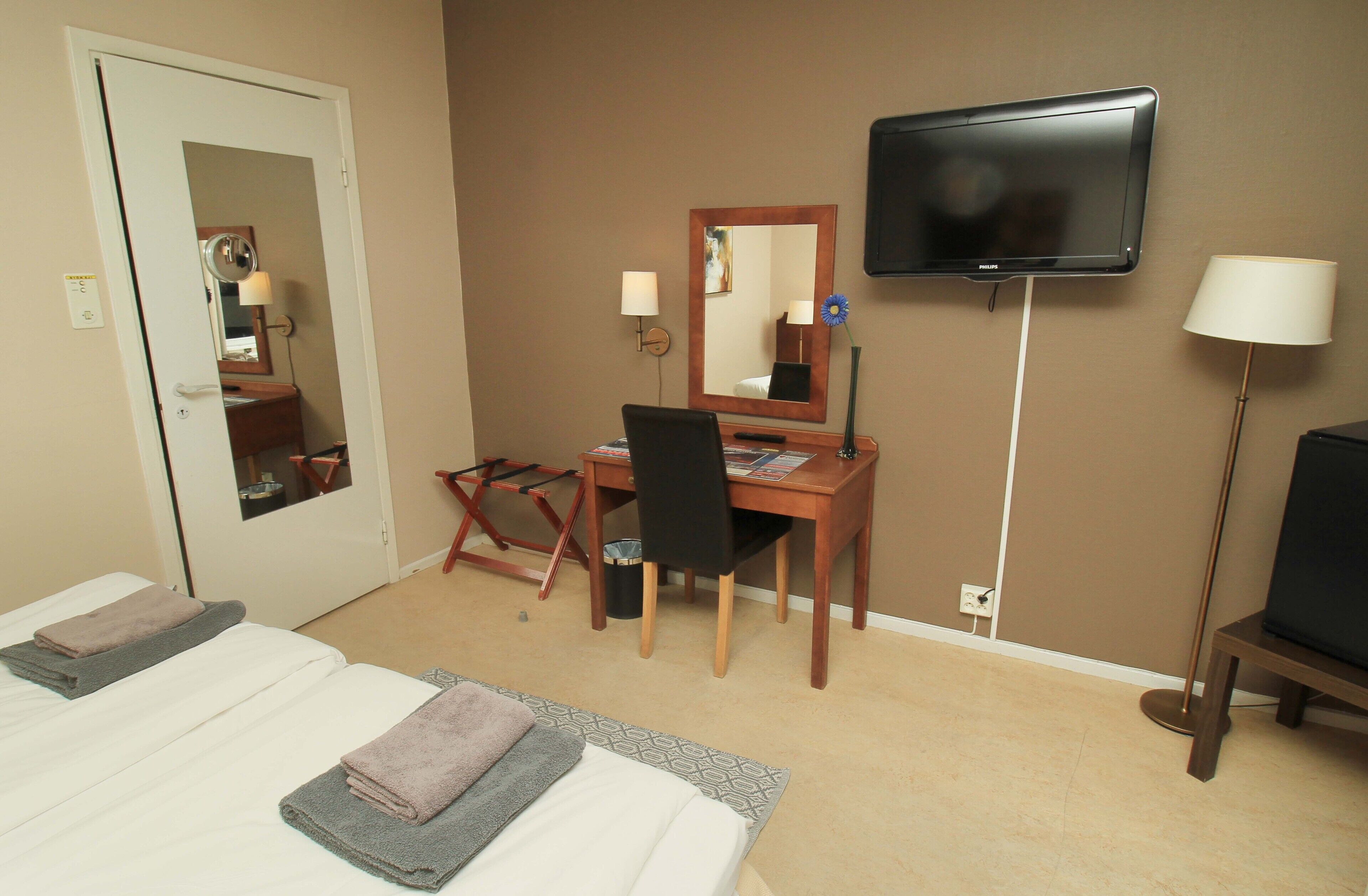 Une chambre d’hôtel équipée d’un lit, d’un bureau, d’une chaise, d’une télévision et d’un miroir.