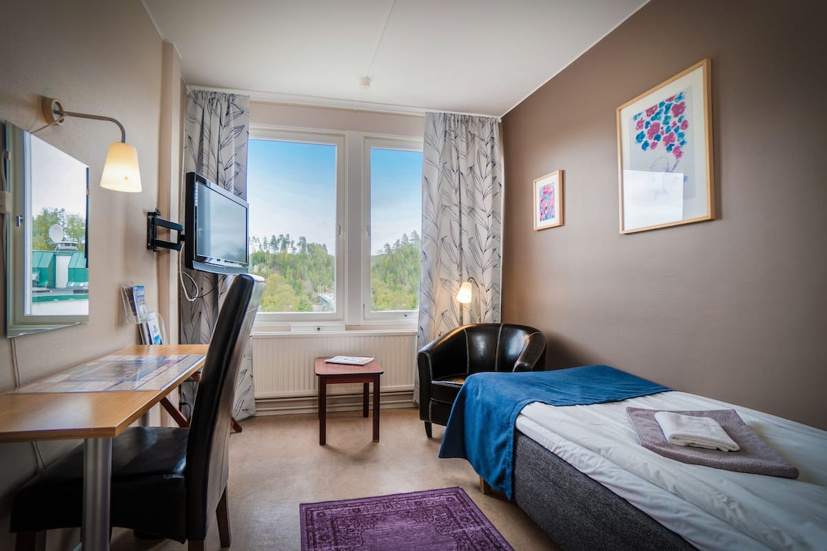 A hotel room with a bed, a desk, a chair, a TV, and a window with curtains.