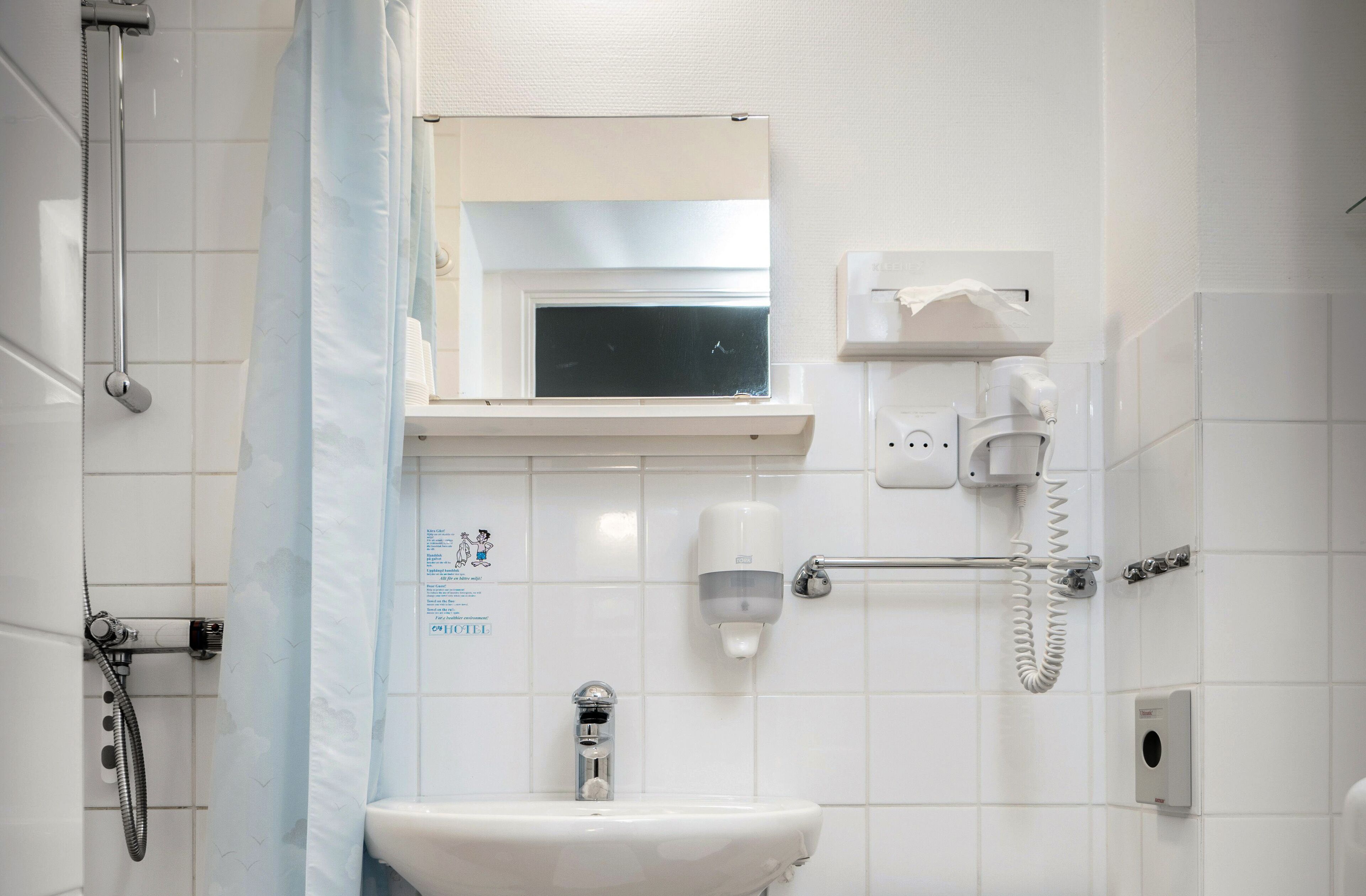 Een badkamer met een douche, wastafel, spiegel en handdroger.