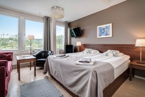A hotel room with a large bed, a desk, a chair, a TV, and a view of the outdoors. - Hotel Sollefteå (Solleftea)