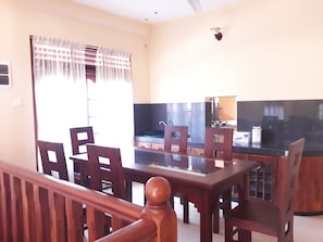 A dining area with a wooden table and chairs, a television, and a kitchen area in the background. - Vinses Villa in Hikkaduwa (Gonapinuwala)