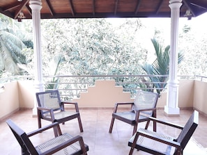 A covered balcony with four wooden chairs and a white balustrade. - Vinses Villa in Hikkaduwa (Gonapinuwala)