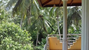 Un balcon abrité offrant une vue sur un jardin luxuriant et des palmiers.