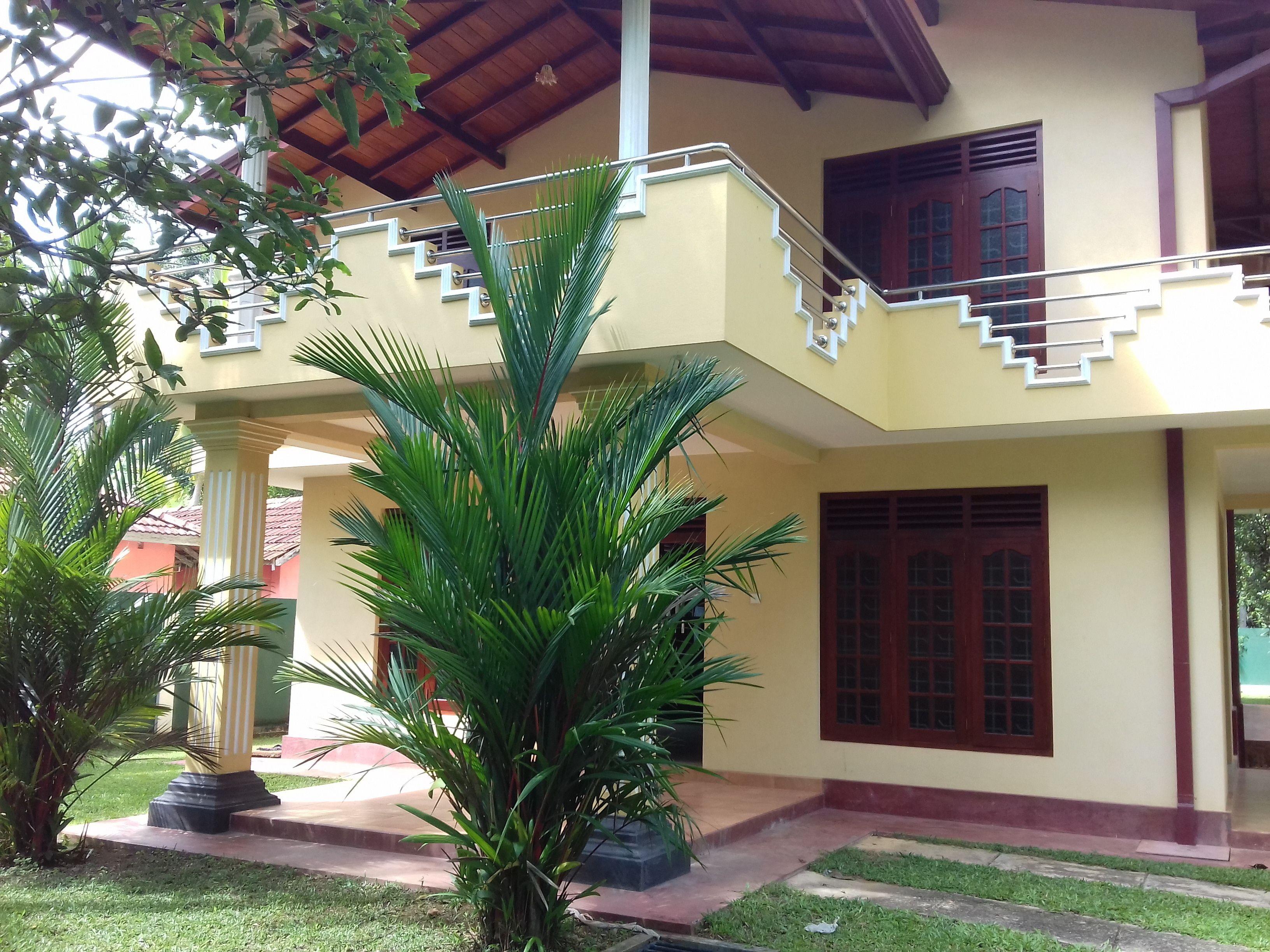 A two-story building with a balcony, a staircase, and a garden area with palm trees.