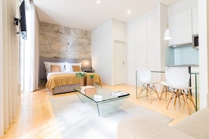 Une chambre moderne avec un mur d’accent en pierre, une table basse en verre, un lit recouvert d’une courtepointe à carreaux jaunes et blancs, et une petite table de chevet agrémentée d’une plante.