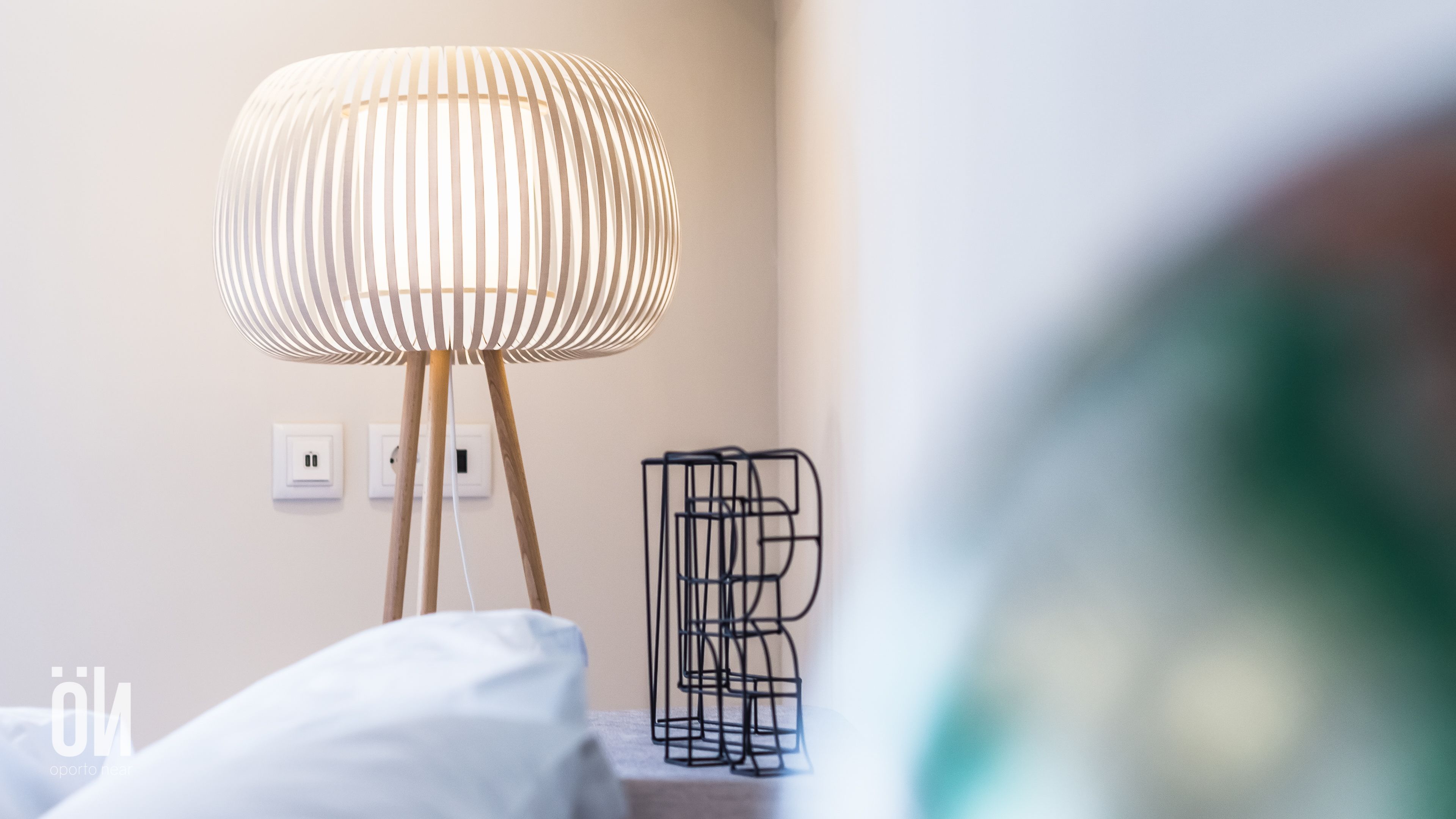 A modern lamp with a ribbed design on a wooden stand, a power outlet, and a black metal sculpture on a table.