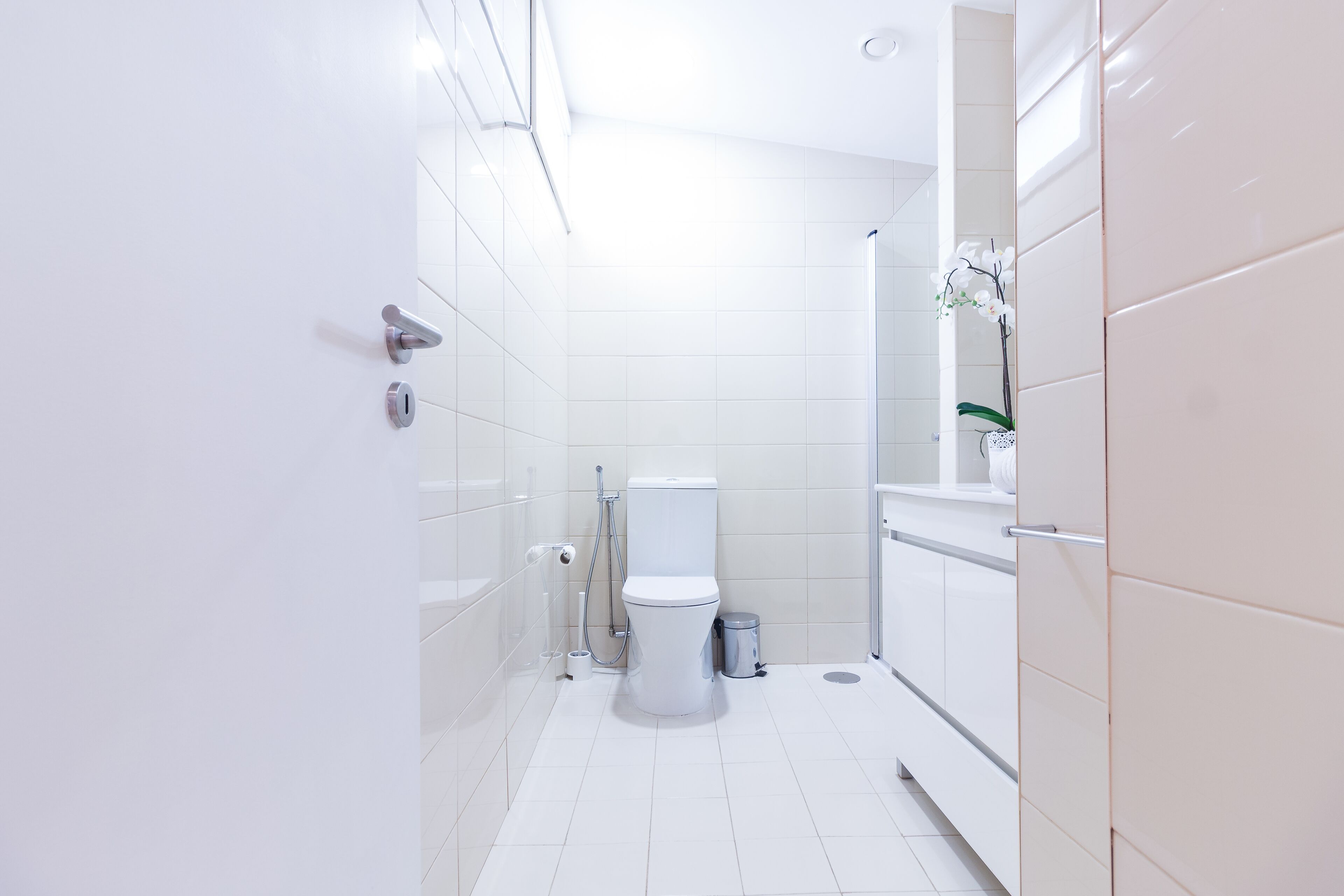 A modern bathroom with white tiles, a toilet, a shower, and a sink.