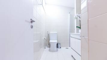A modern bathroom with white tiles, a toilet, a shower, and a sink.