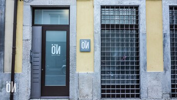 Une façade d’immeuble avec une porte marron, une fenêtre à vitre dépolie et une fenêtre avec un grillage métallique.