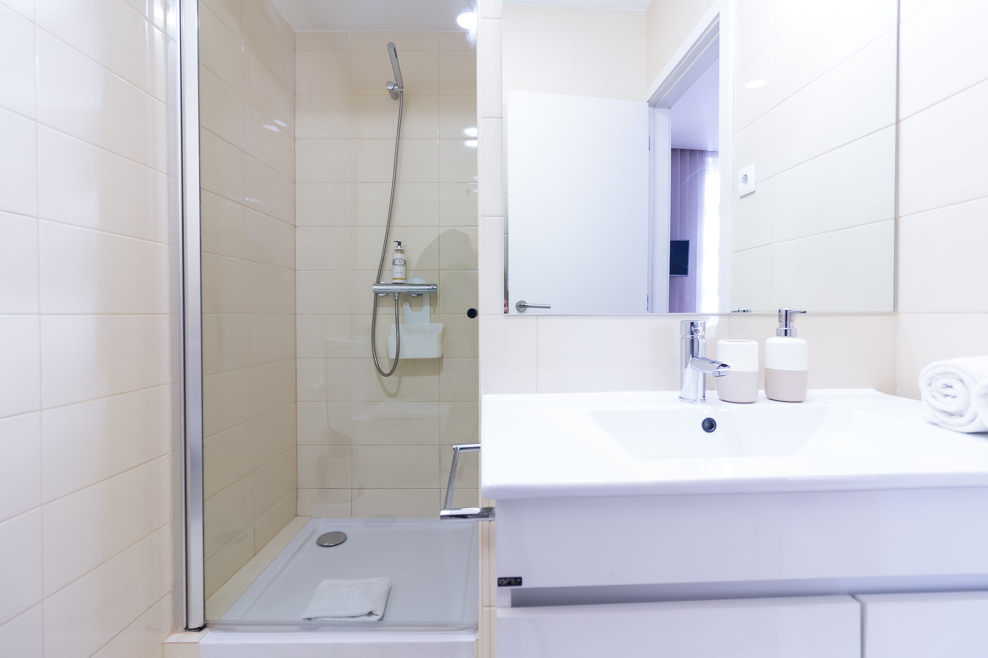 A modern bathroom with a glass-enclosed shower, a white sink with toiletries, and a large mirror.