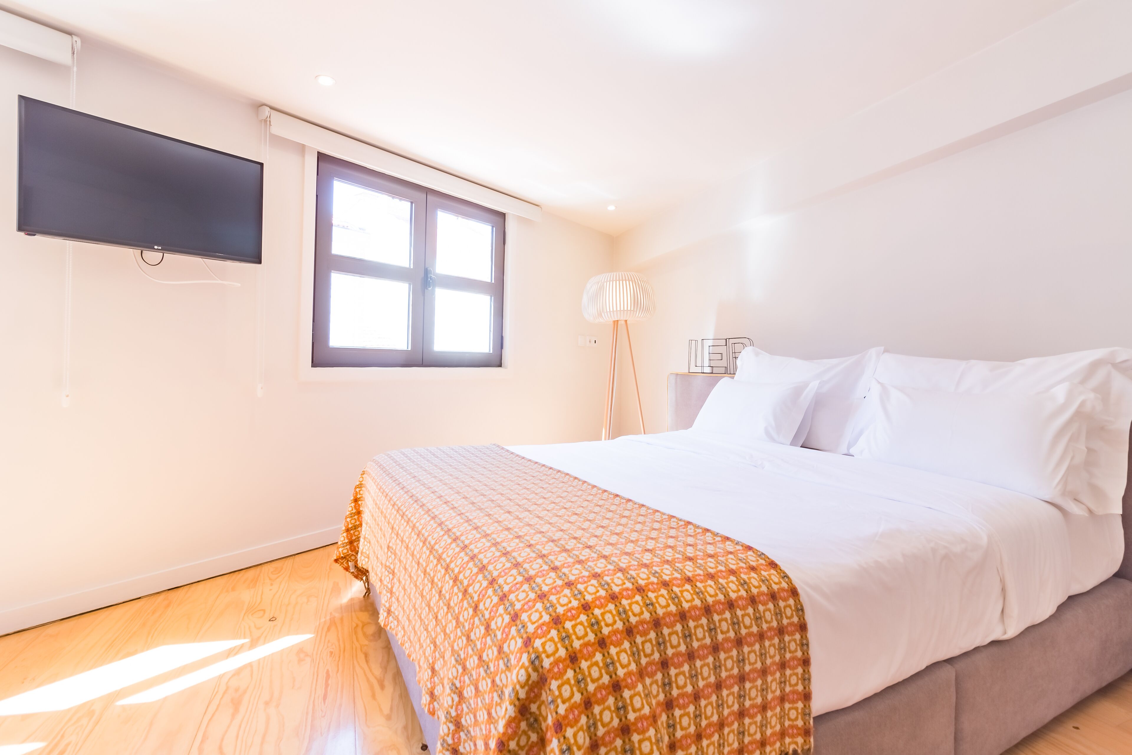 Une chambre à coucher avec un lit, un téléviseur fixé au mur, une fenêtre et une lampe sur pied.