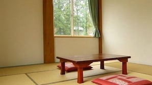 Ein Zimmer mit Tatami-Boden, einem niedrigen Holztisch und einem Fenster mit grünen Vorhängen.