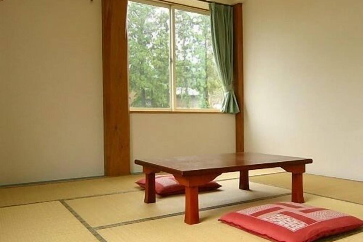 Une pièce avec un sol recouvert de tatamis, une petite table en bois et une fenêtre ornée de rideaux verts.