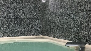 Ein rechteckiges Whirlpool-Becken mit weißem Innenraum, vor einer dunklen Granitwand.