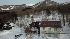 A two-story house with a steep roof, surrounded by snow-covered trees and mountains in the background. - PENSION Sanrinsya (Shizukuishi)