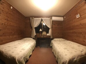 A small, cozy room with two single beds, a desk with a mirror, and an air conditioning unit on the wall. - PENSION Sanrinsya (Shizukuishi)