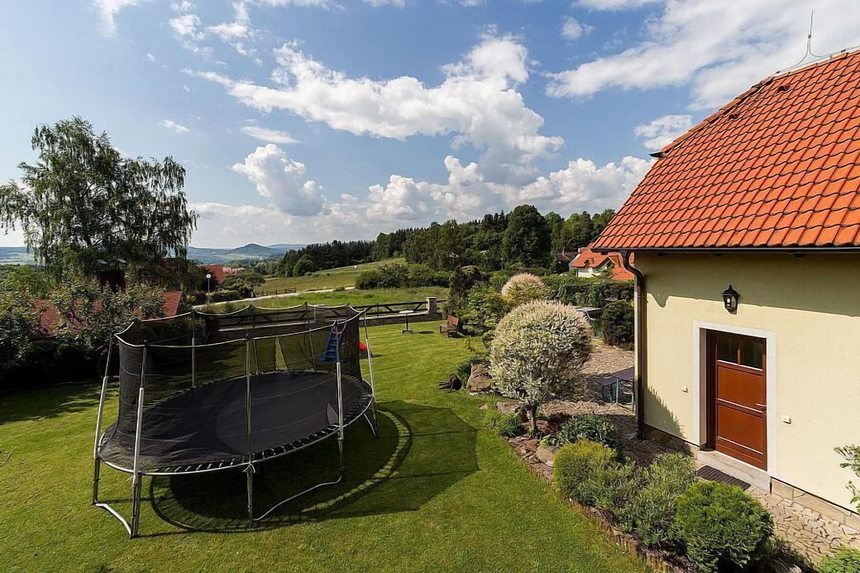 A house with a red-tiled roof, a trampoline in the backyard, and a well-maintained lawn.
