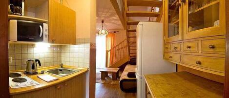 A compact kitchen with wooden cabinets, a microwave, a kettle, and a built-in stove.