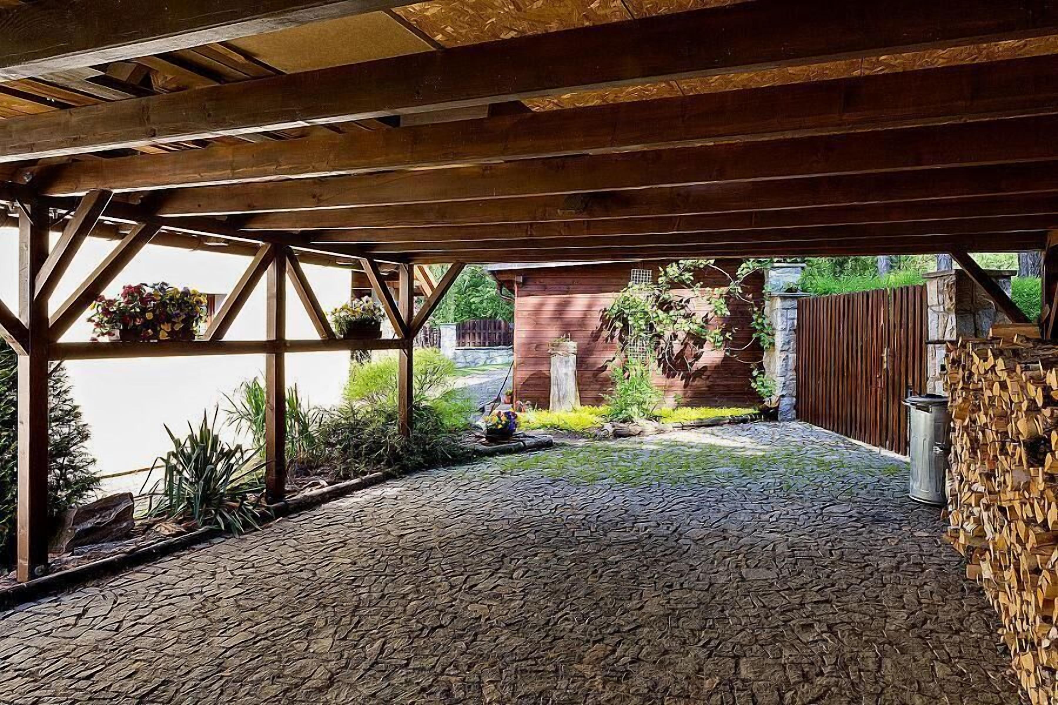 A covered outdoor area with a brick pathway, wooden beams, and potted plants.