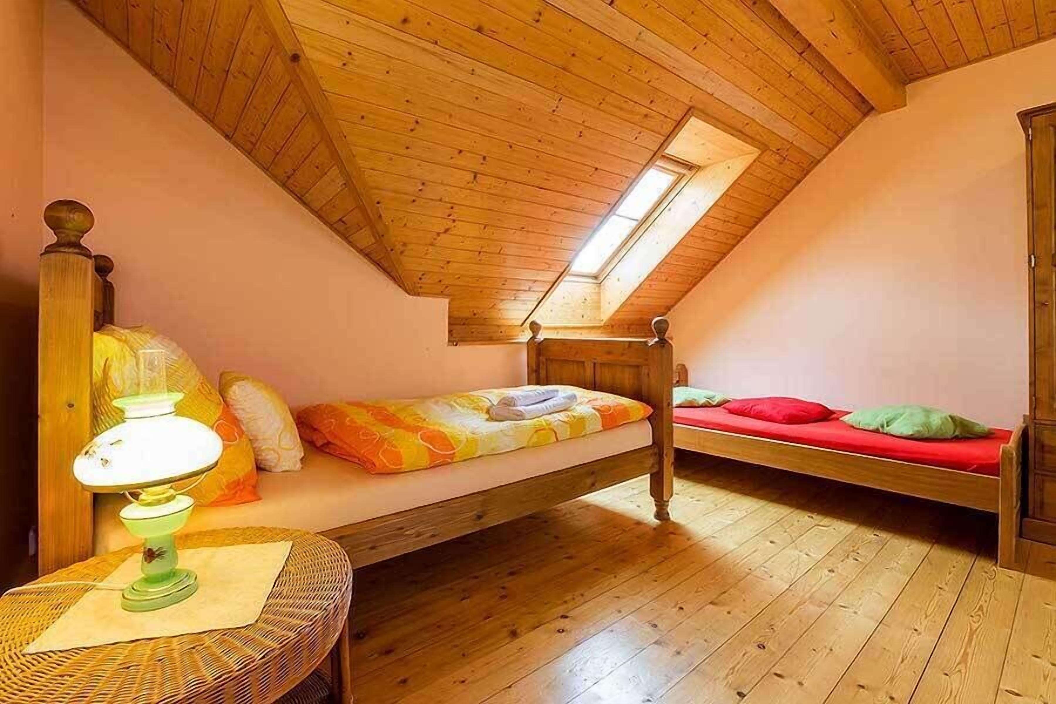 A small attic bedroom with two wooden beds, a table with a lamp, and a skylight.