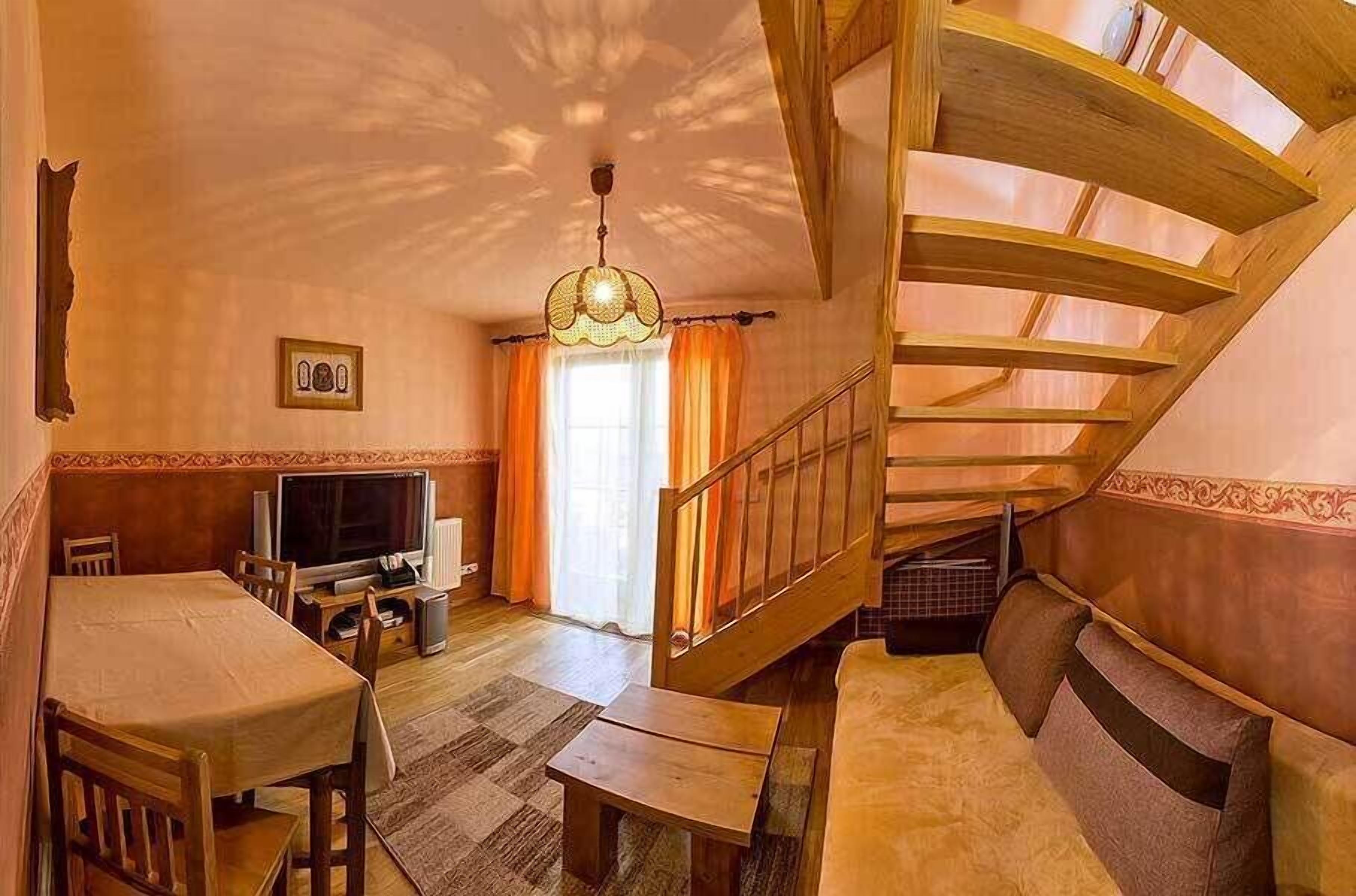 A cozy room with a wooden staircase, a television, a dining table, and a sofa.