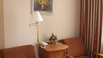 A hotel room with a brown sofa, a wooden side table with a lamp, a telephone, and a painting of sunflowers on the wall.