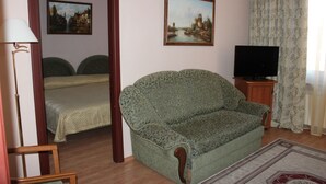 A room with a sofa, a television on a wooden stand, a bed with green bedding, and two paintings on the wall. - Domus Hotel -1 (Kyiv)