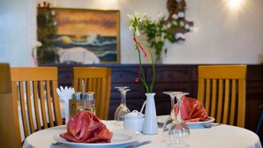A dining table set with plates, cutlery, a vase with flowers, and a painting on the wall. - Domus Hotel -1 (Kyiv)