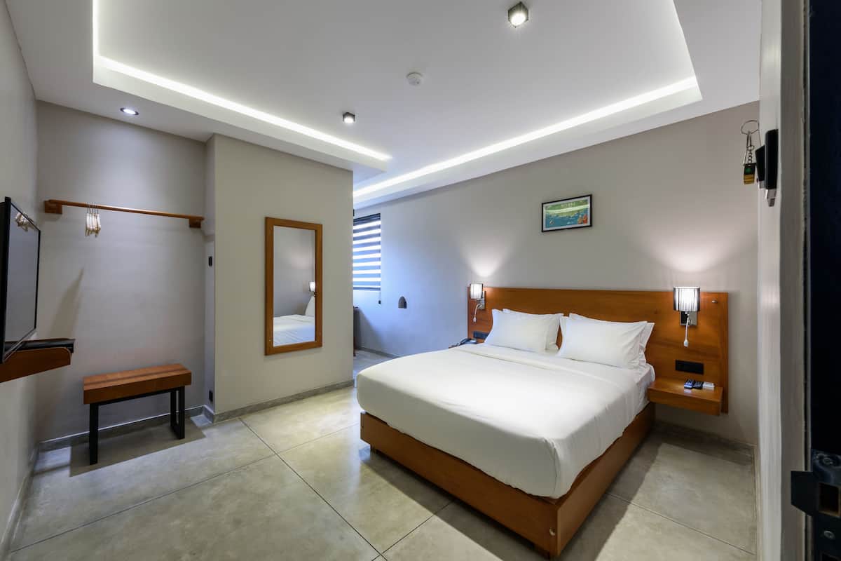 A hotel room with a large bed, bedside tables, a bench, a mirror, and recessed ceiling lighting.