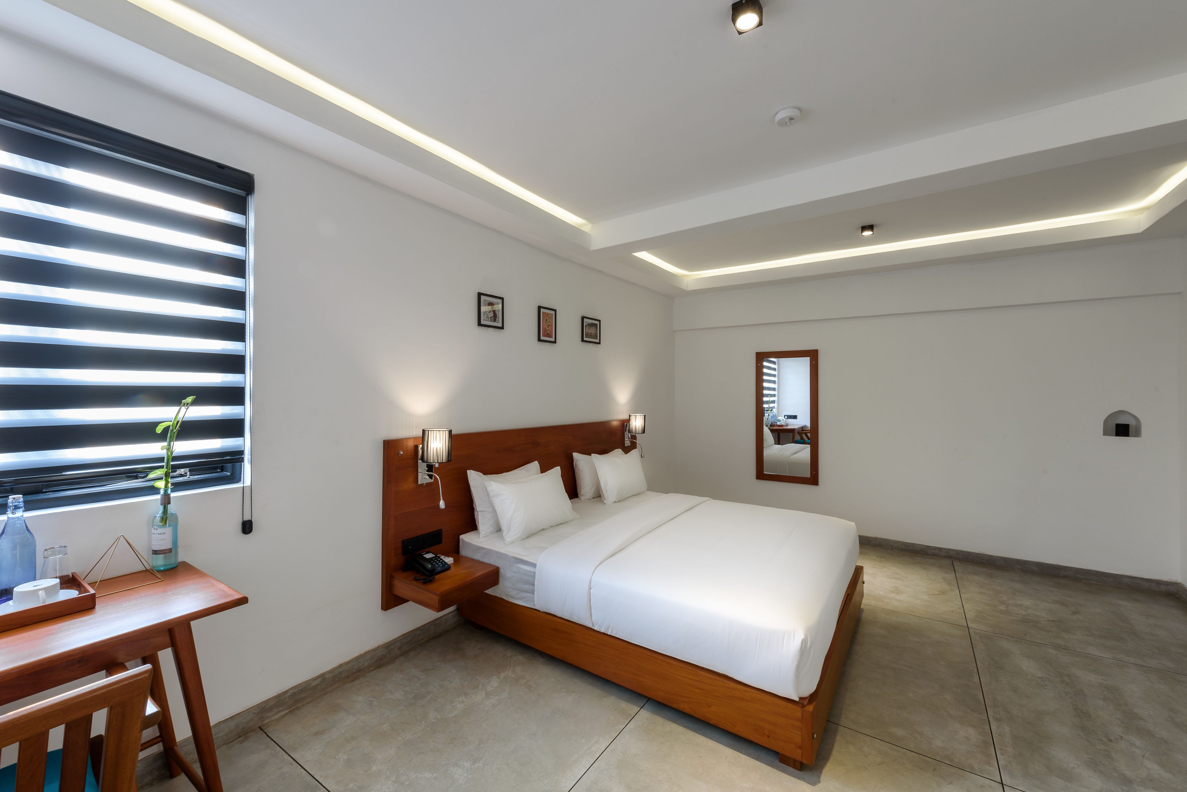 Una habitación de hotel moderna con una cama grande, mesitas de noche, un escritorio y una ventana con persianas.