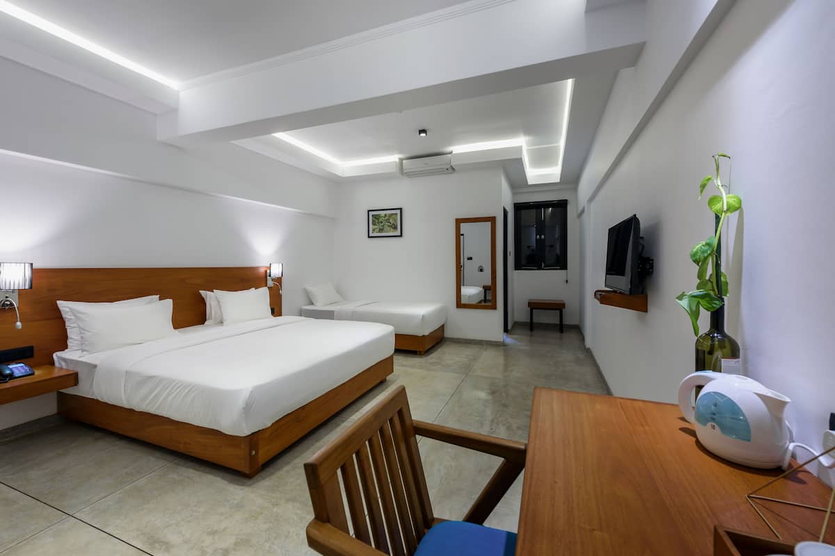 A modern hotel room with a large bed, a wooden desk, a chair, a TV, and a plant.