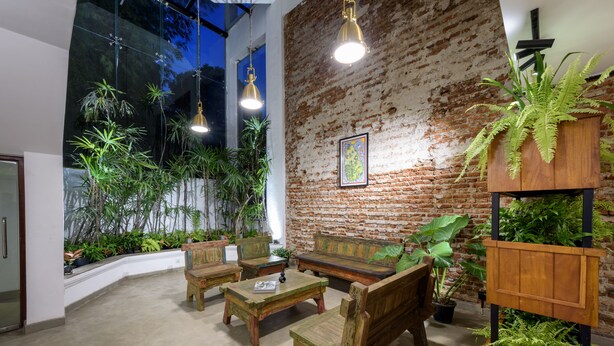 A cozy indoor space with a rustic brick wall, wooden furniture, and lush green plants. - Fern Colombo (Colombo)