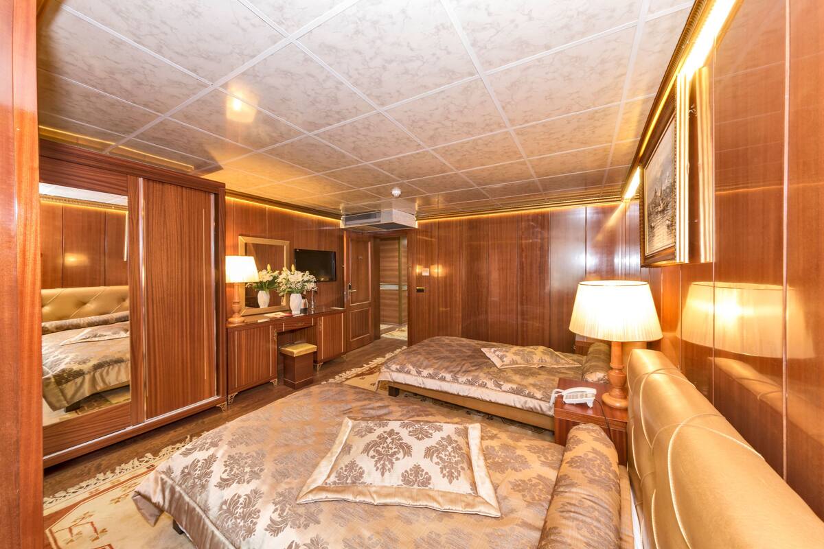 A hotel room with two beds, wooden paneling, a mirror, a desk with a lamp, and a telephone.