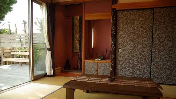 Una habitación japonesa tradicional con suelo de tatami, una mesa de madera baja, puertas correderas shoji y vistas a una terraza de madera.