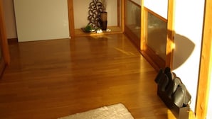 Una habitación japonesa tradicional con suelo de madera, un tatami, una estantería con adornos y una puerta corredera.