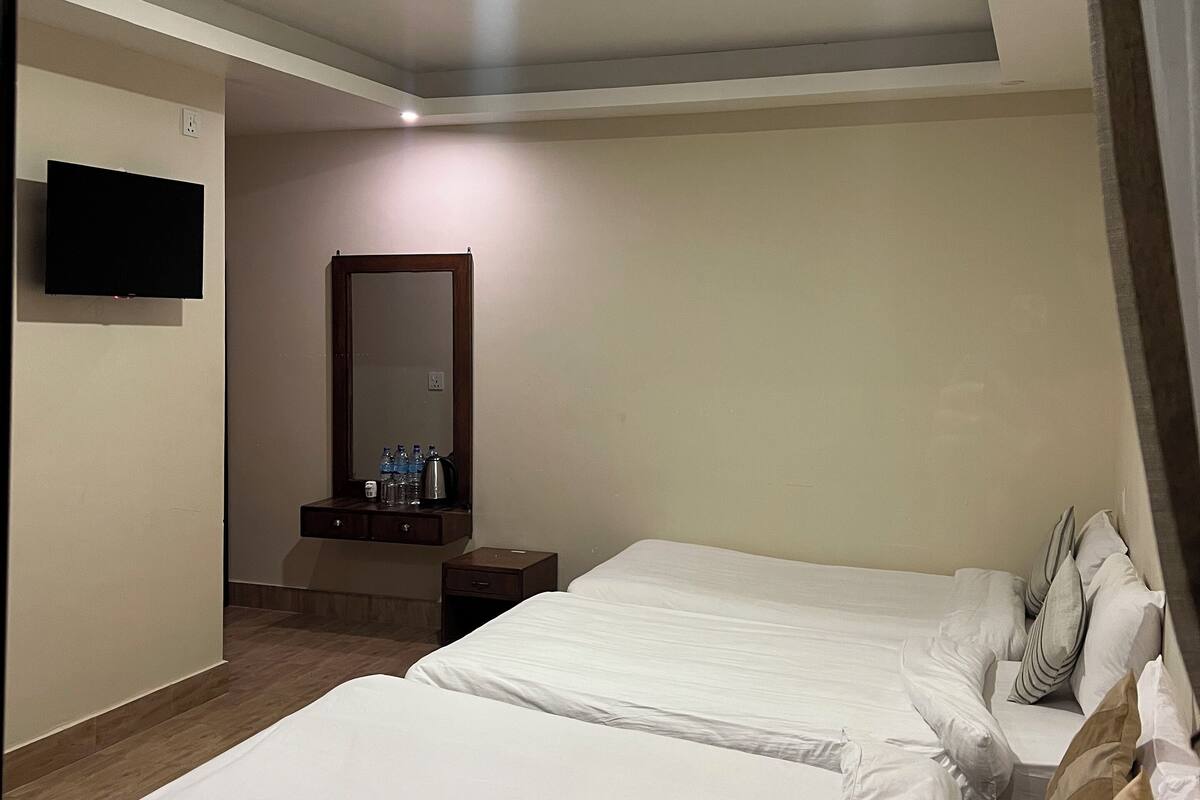 A hotel room with two beds, a flat-screen TV mounted on the wall, a small table with a mirror, and a nightstand.