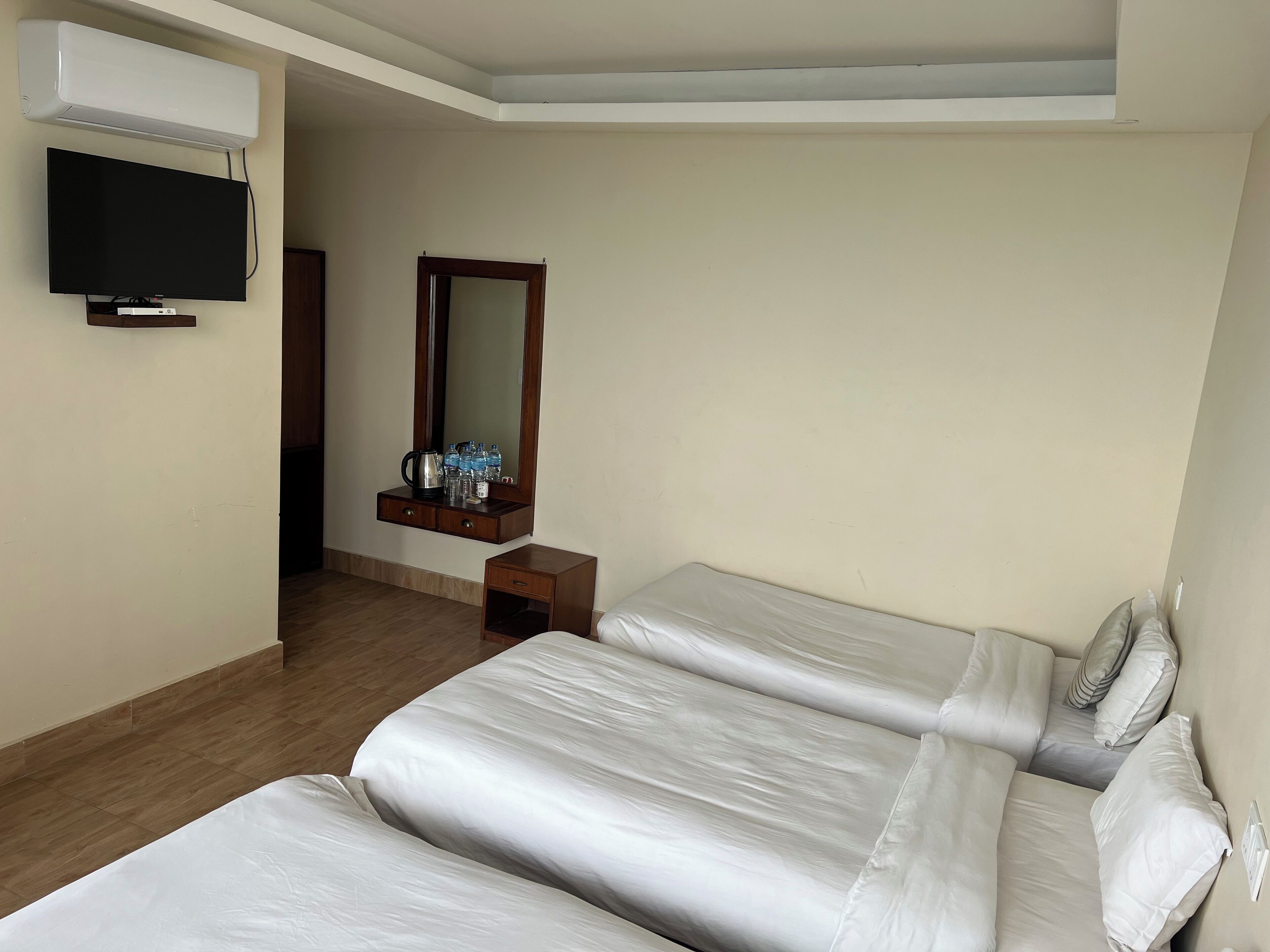 A hotel room with two beds, a TV, a mirror, and a small table with a kettle and bottles.