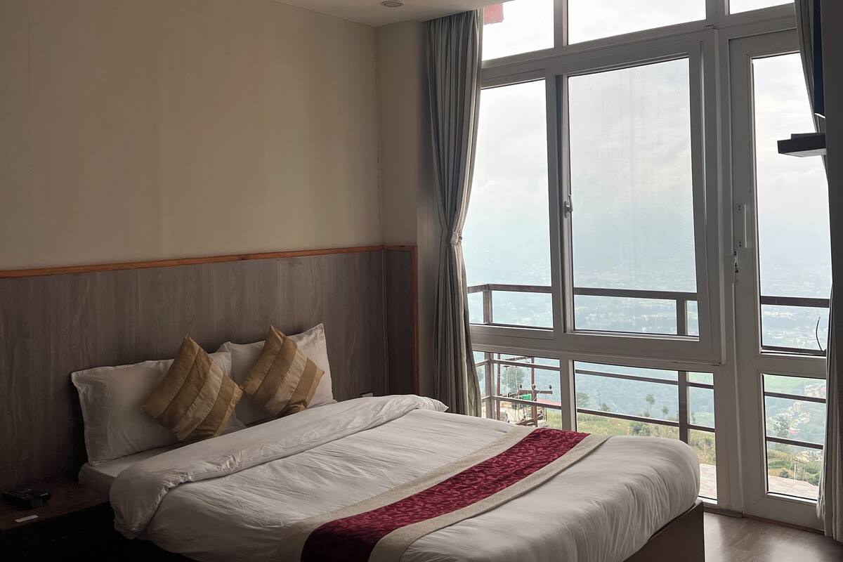 A bedroom with a large bed, a wooden headboard, and a view of a cityscape through large windows.
