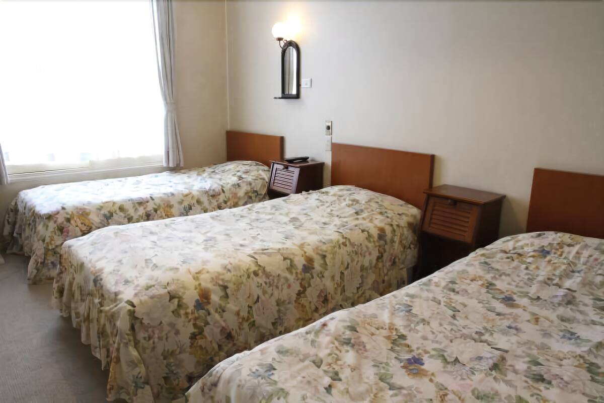 A hotel room with two single beds, a nightstand, a wall-mounted mirror, and a window with curtains.