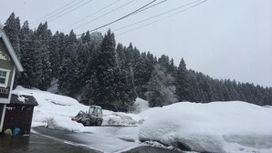Un paysage enneigé avec un bâtiment et une machine à déneiger qui dégage une route.