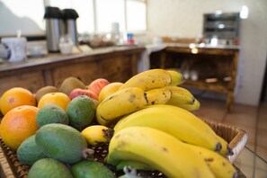 A fruit basket with bananas, oranges, and limes on a glass table in a kitchen. - Casa das Proteas (Santana)