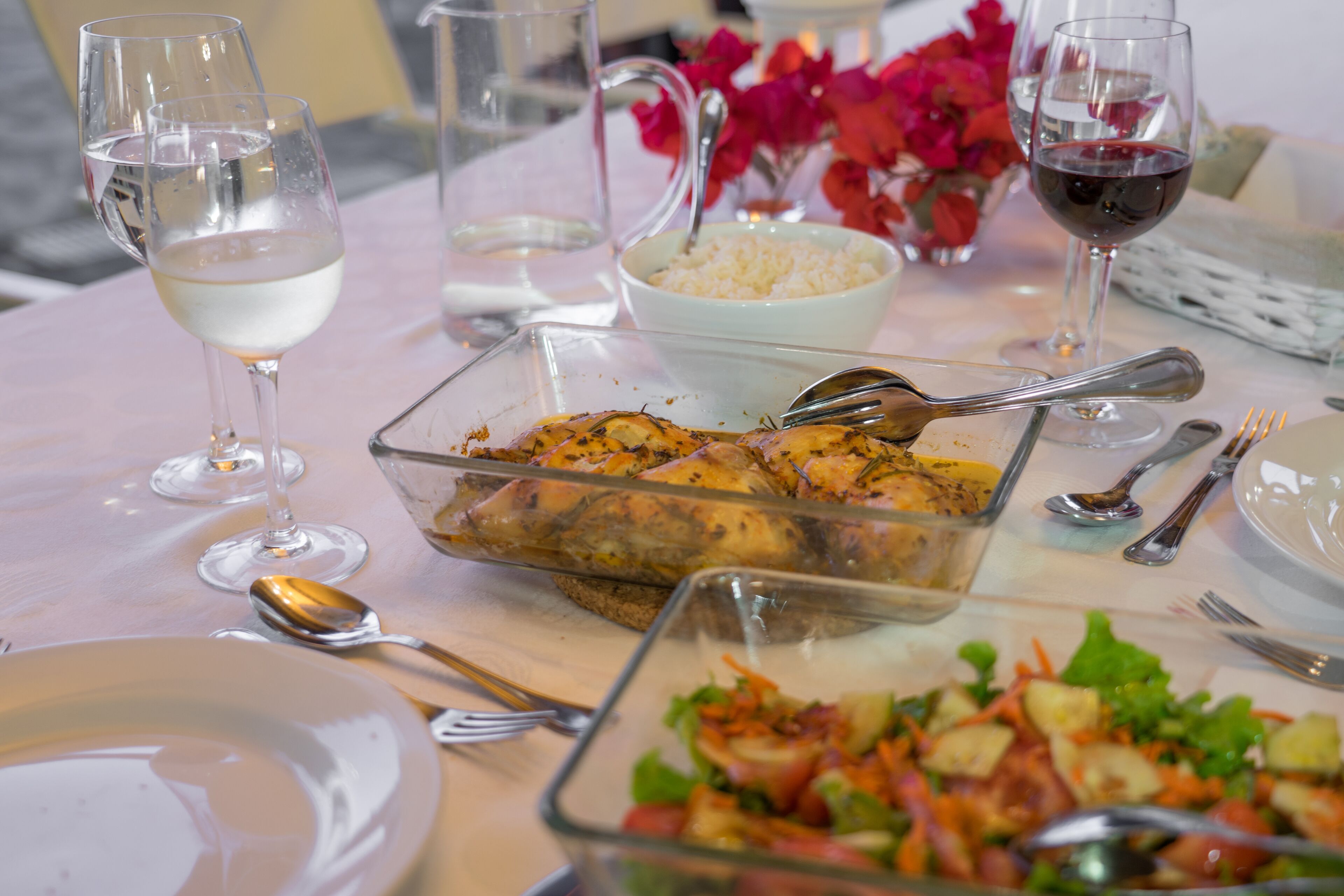 A dining table set with plates, glasses, cutlery, and a variety of dishes including a salad and roasted chicken.