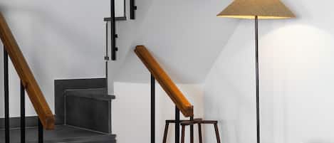 A staircase with black railings and wooden handrails, a standing lamp, and a wicker chair with a white cushion.