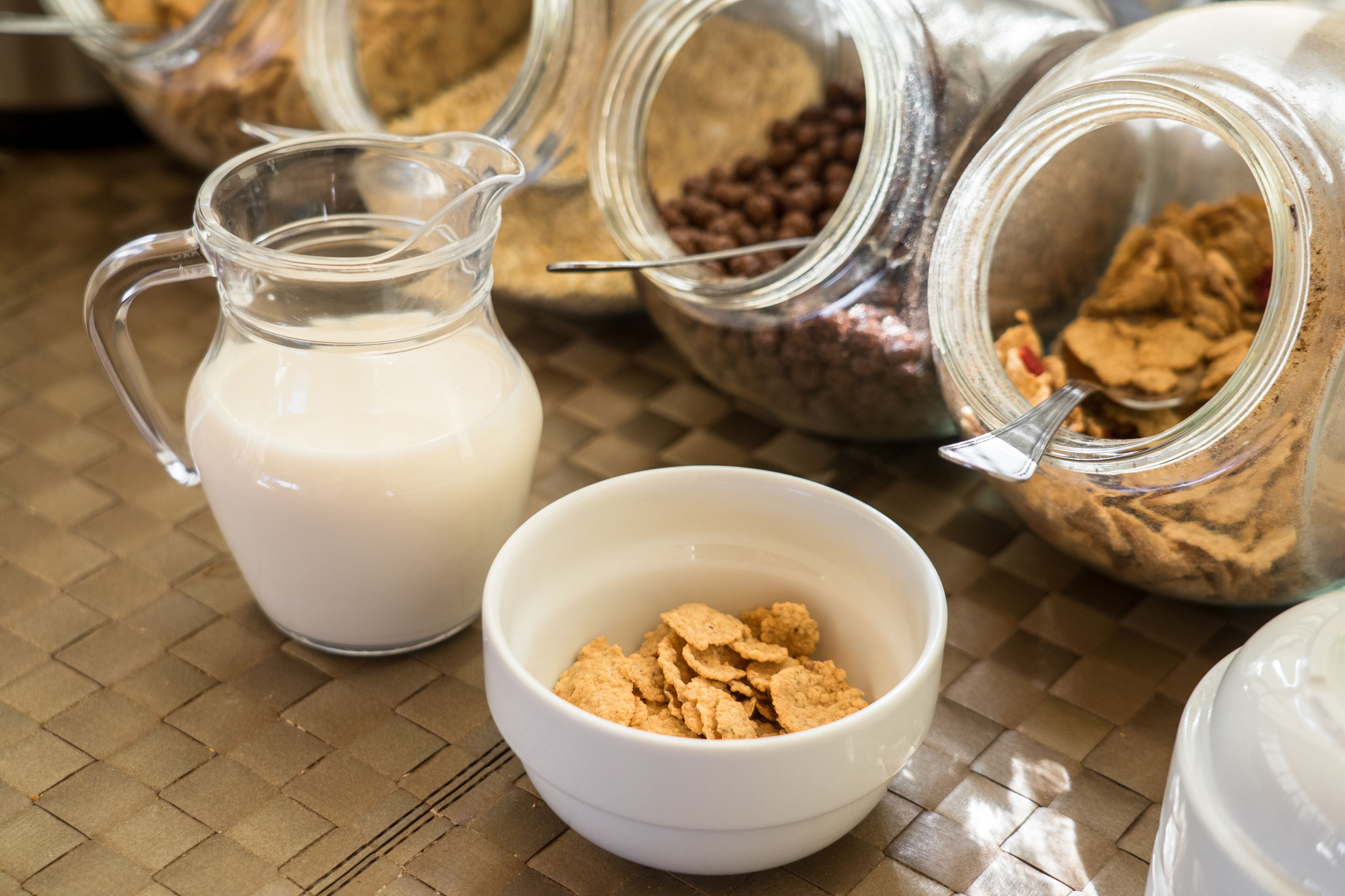 A kitchen area with a pitcher of milk, a bowl of cereal, and jars of ingredients.