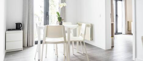 A modern, well-lit room with a dining table and chairs, a radiator, and a view of the outdoors through large windows.
