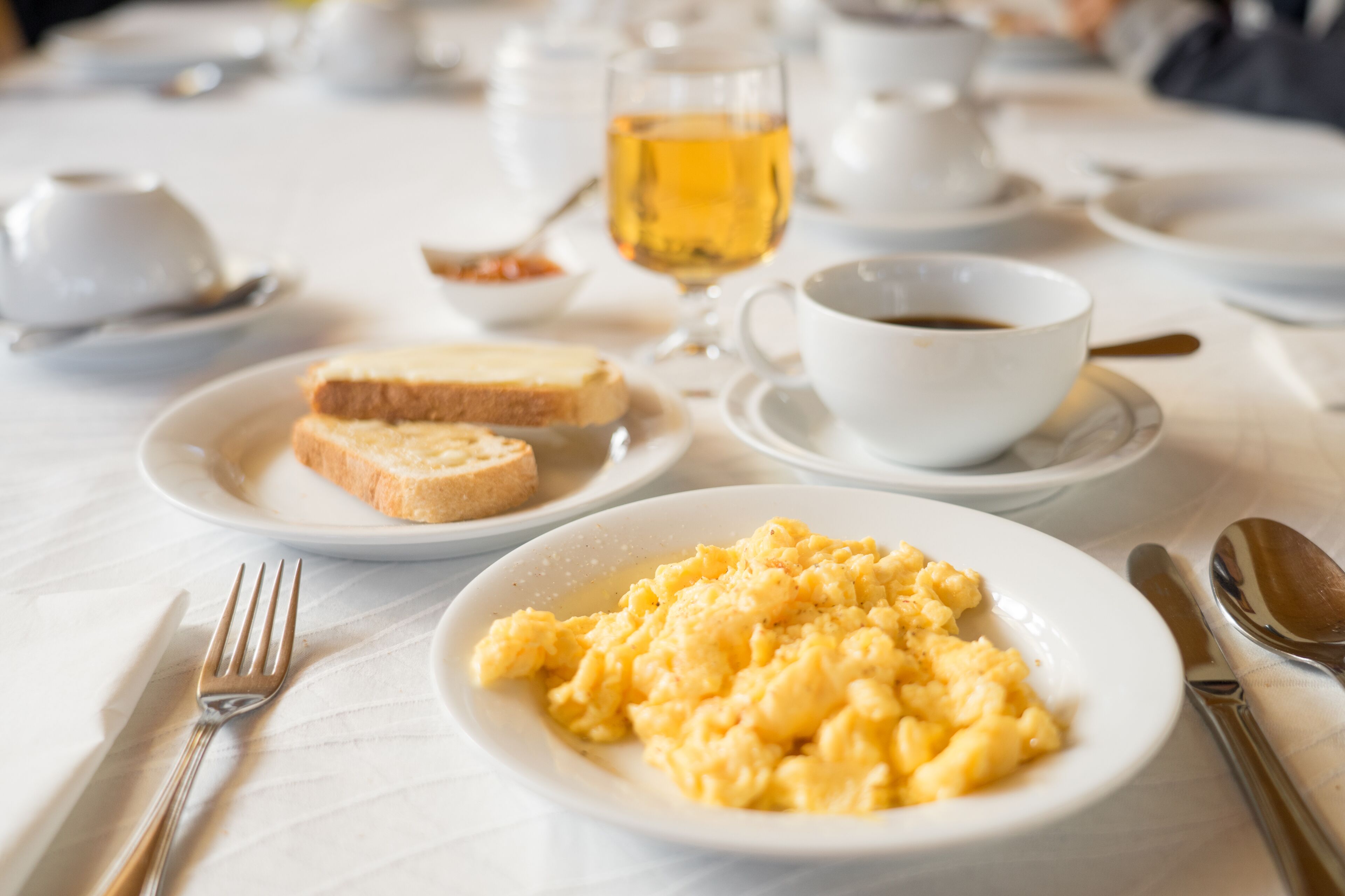 Una colazione con uova strapazzate, pane tostato, caffè e tè su un tavolo.